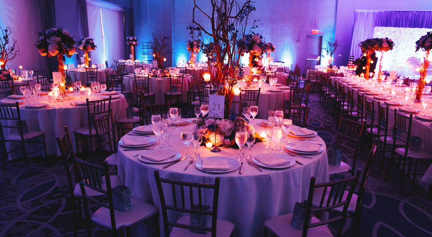 Große Fest- und Hochzeitstafel mit vielen Stühle und Tischen und eine große Hochzeitsgesellschaft mit Licht in Szene gesetzt.
