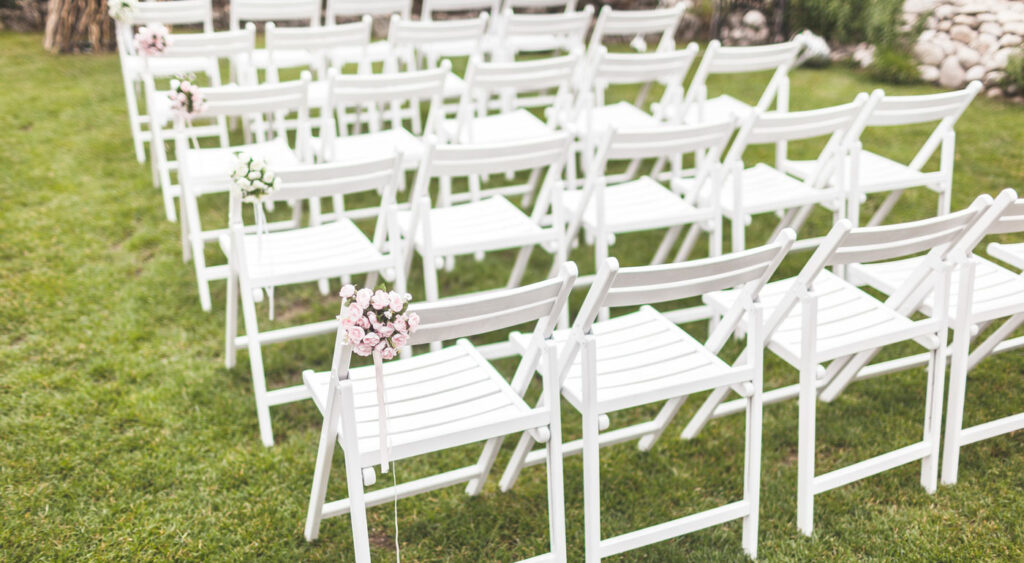 Outdoor Hochzeit mit dekorierten weißen Stuhlreihen passender Hochzeitsstühle.