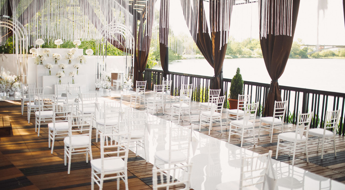 Hochzeit in Weiß mit weißen Chiavari Stühlen direkt an einem See.